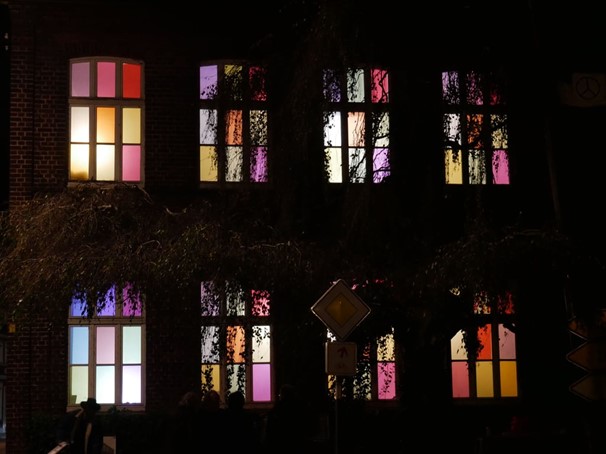 Die "Rote Schule" In Albersloh von vorne. Es ist dunkel und alle Fenster sind bunt beleuchtet (Aktion zum Advent).